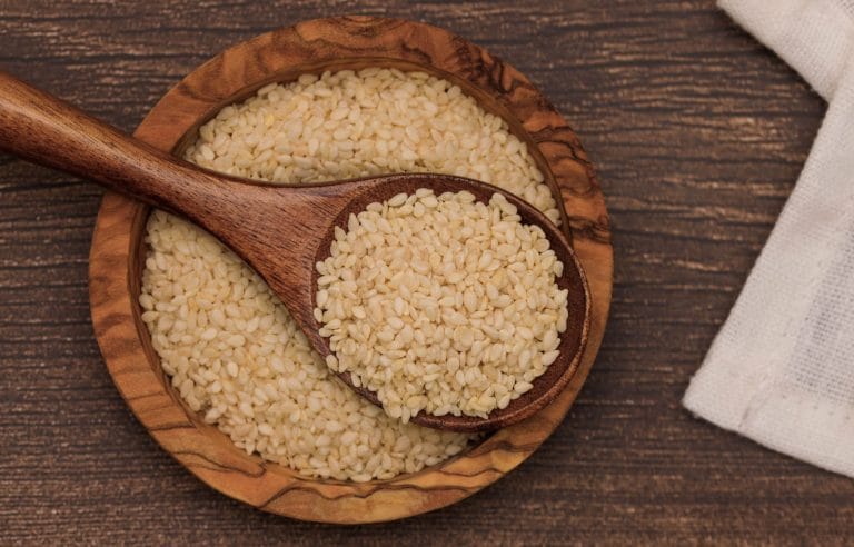 Pale golden sesame seeds piled on a metal spoon over a rustic surface