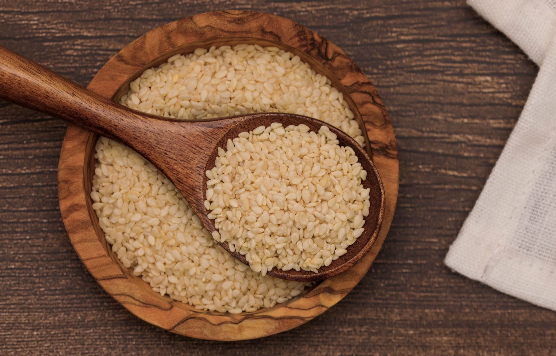 Pale golden sesame seeds piled on a metal spoon over a rustic surface