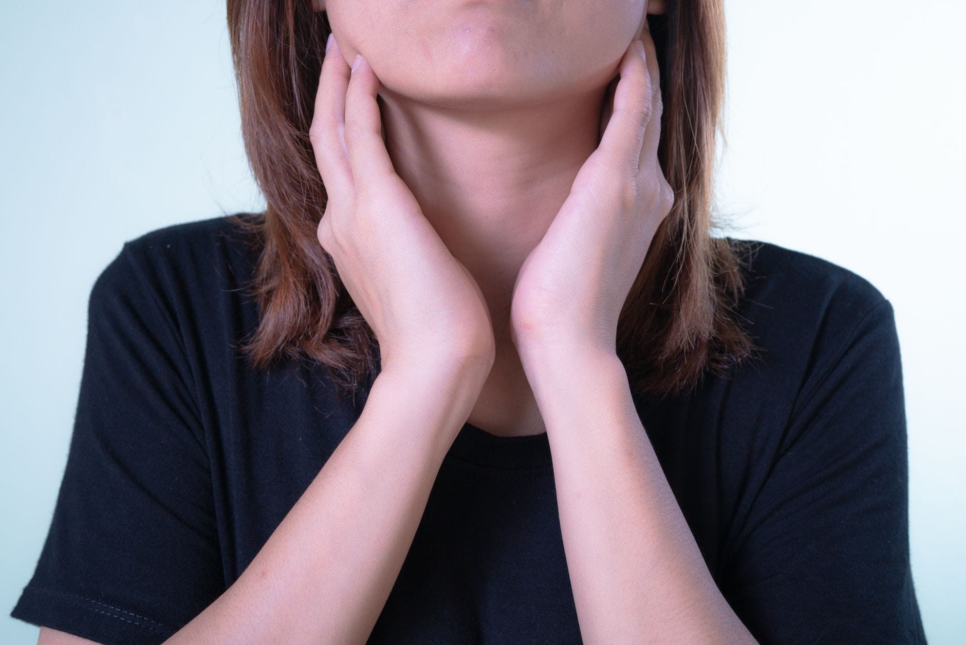 Woman with a scarf holding her neck and wincing in throat discomfort