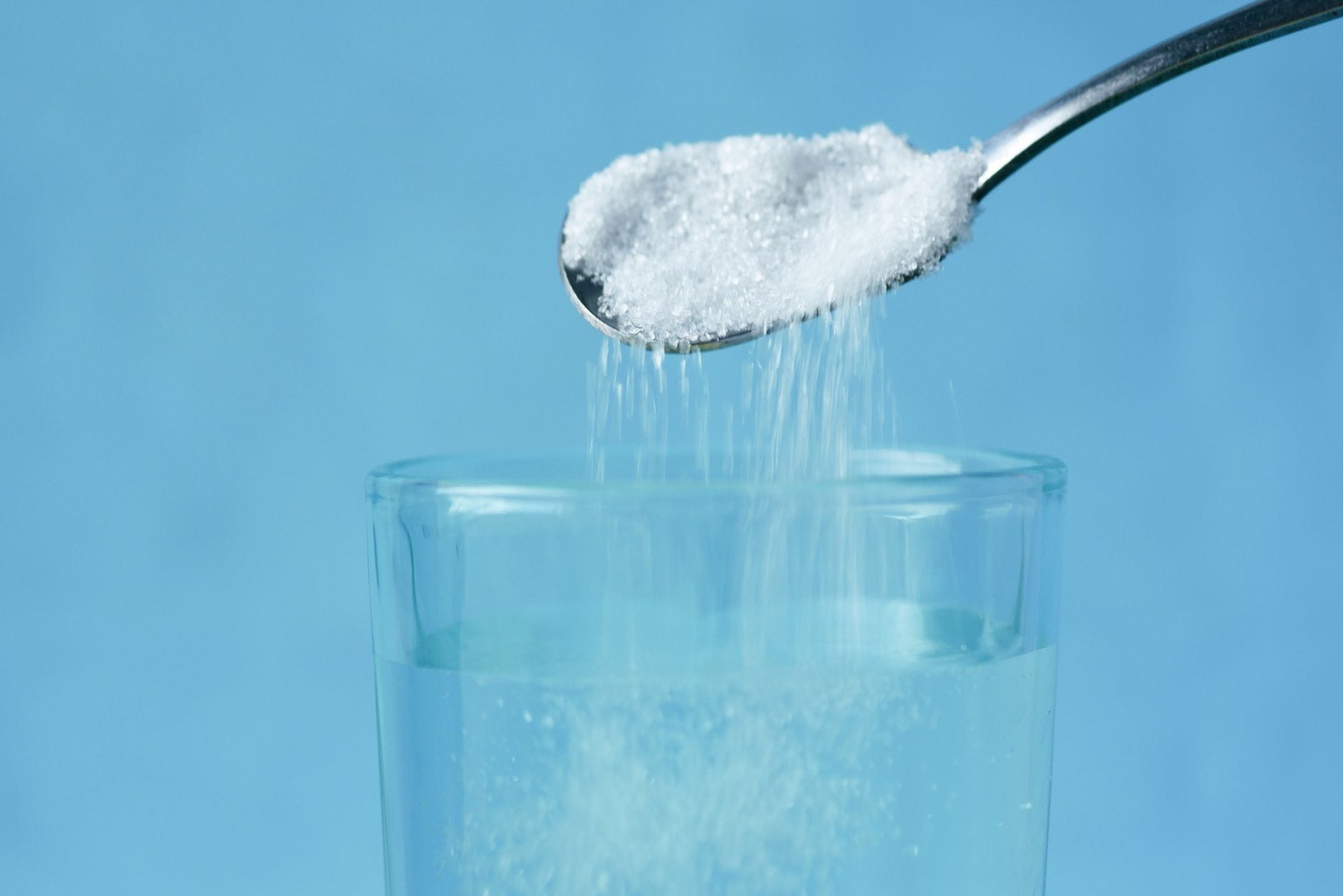 Person mixing salt into a clear glass of warm water beside a spoon