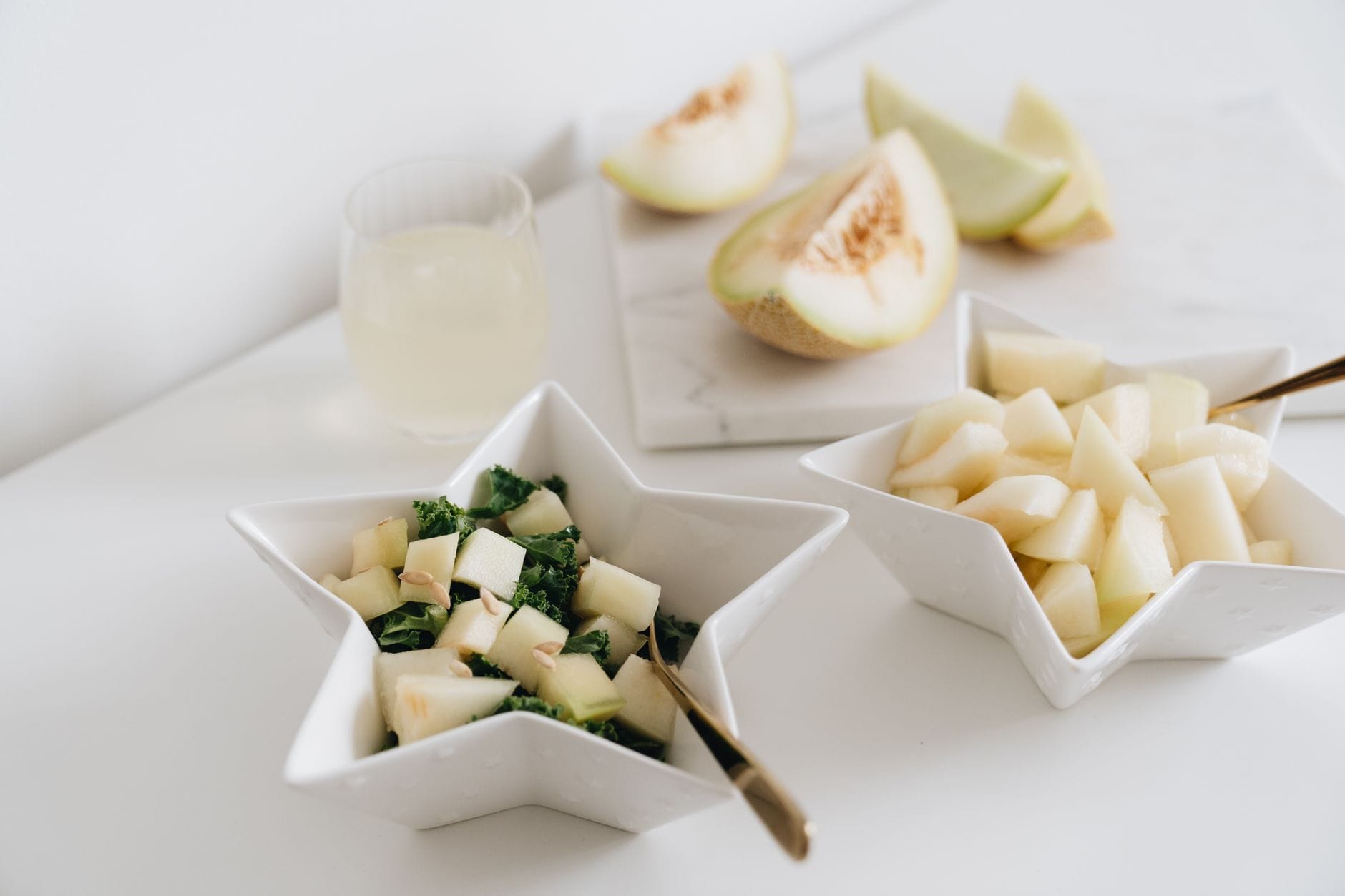 Cubed green and orange melon in a white bowl with a spoon