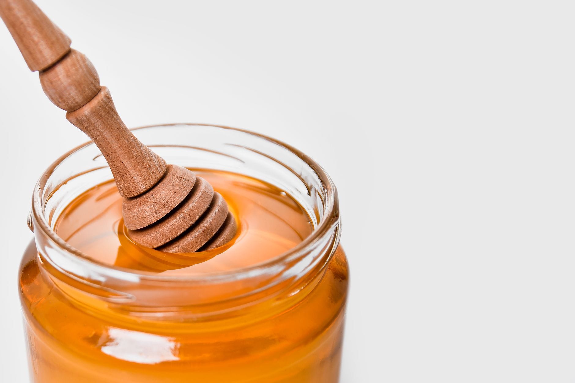 Golden honey dripping from a wooden dipper over an open glass jar