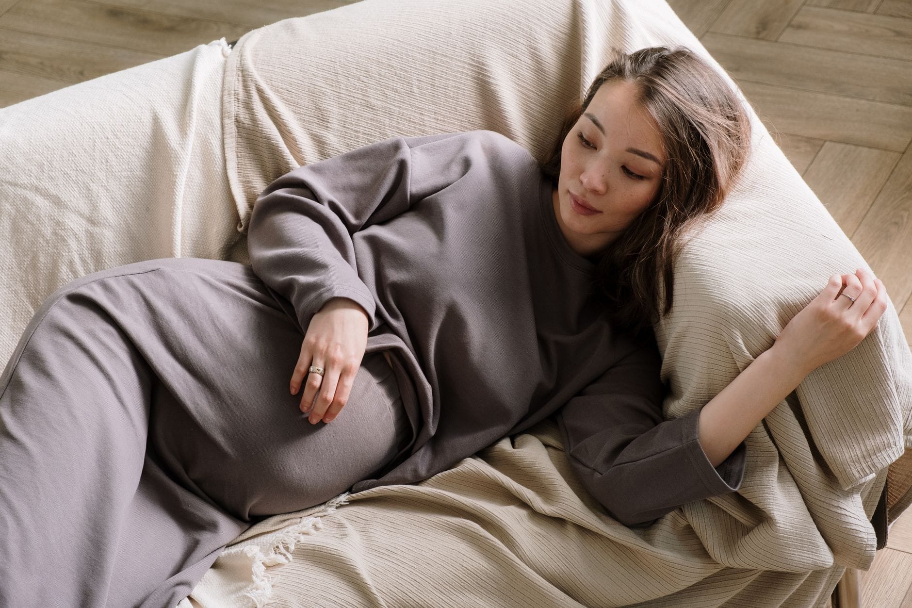 Pregnant woman wrapped in a blanket resting on a sofa holding a warm mug