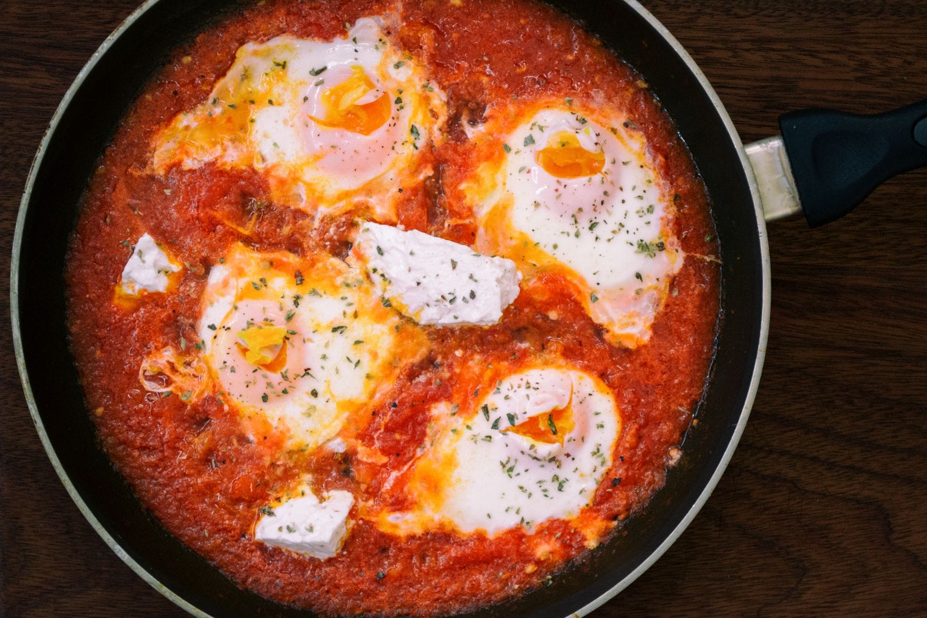 Eggs poaching in a red tomato and pepper sauce in a cast iron skillet