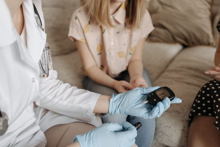A handheld glucose meter showing a reading beside a test strip on a table