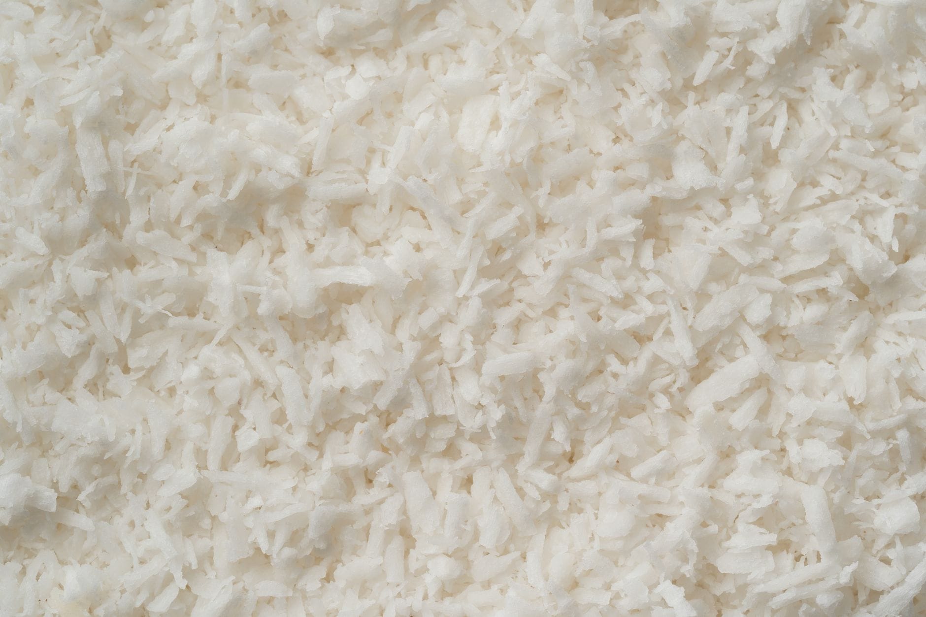 Fine shredded white coconut piled in a ceramic bowl on a pale cloth