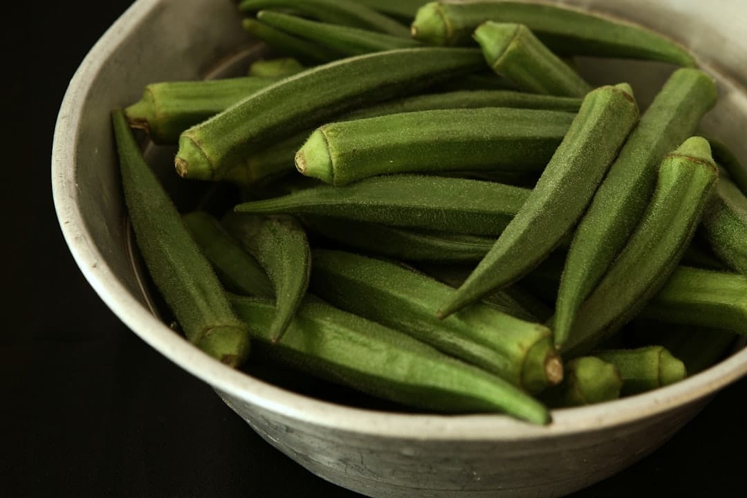 Whole green okra pods piled in a ceramic bowl on a kitchen counter