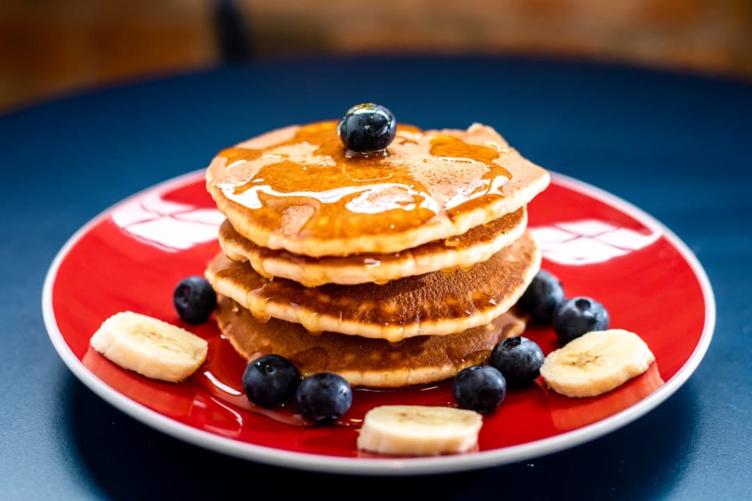 Golden syrup drizzling over a tall stack of pancakes on a white plate