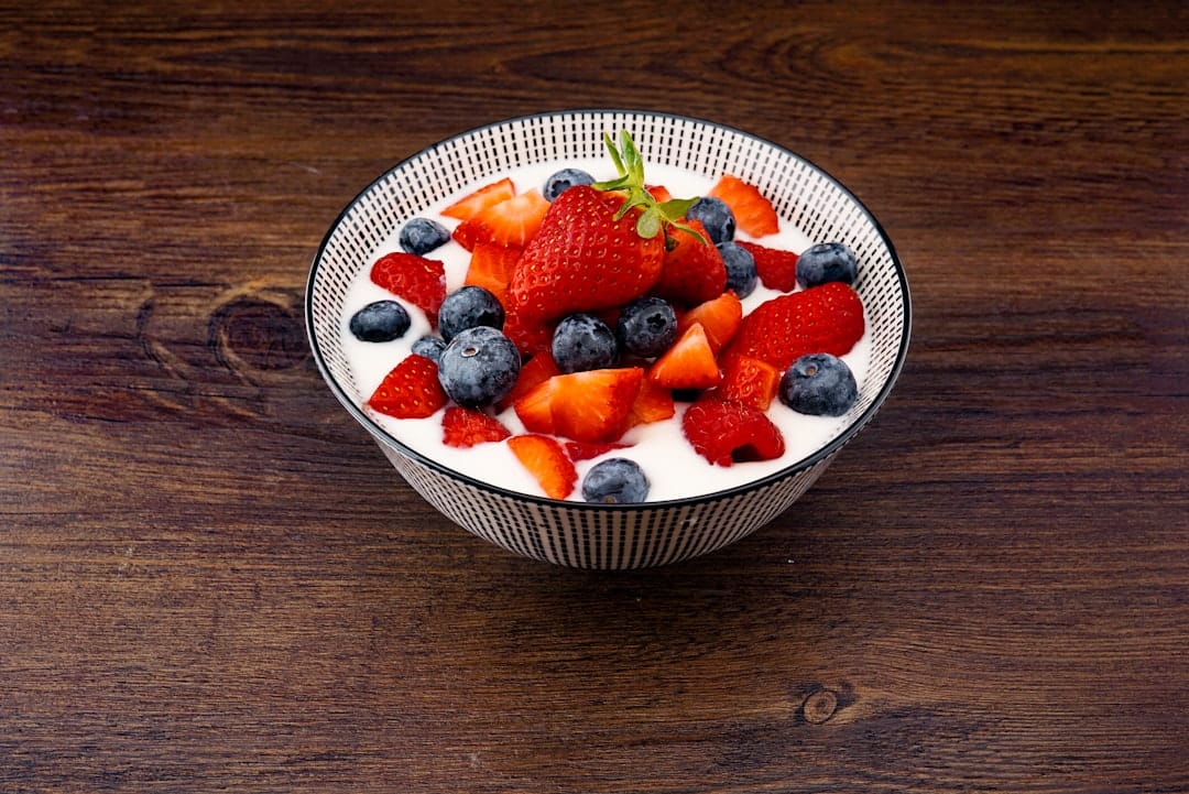 Thick white yogurt topped with blueberries, strawberries and granola in a ceramic bowl