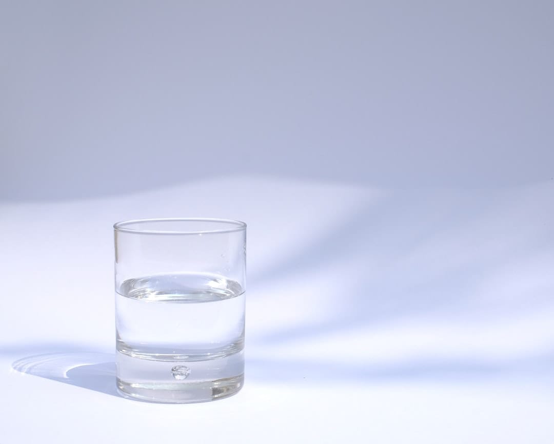 A clear glass of water beside a small pile of coarse salt on a table