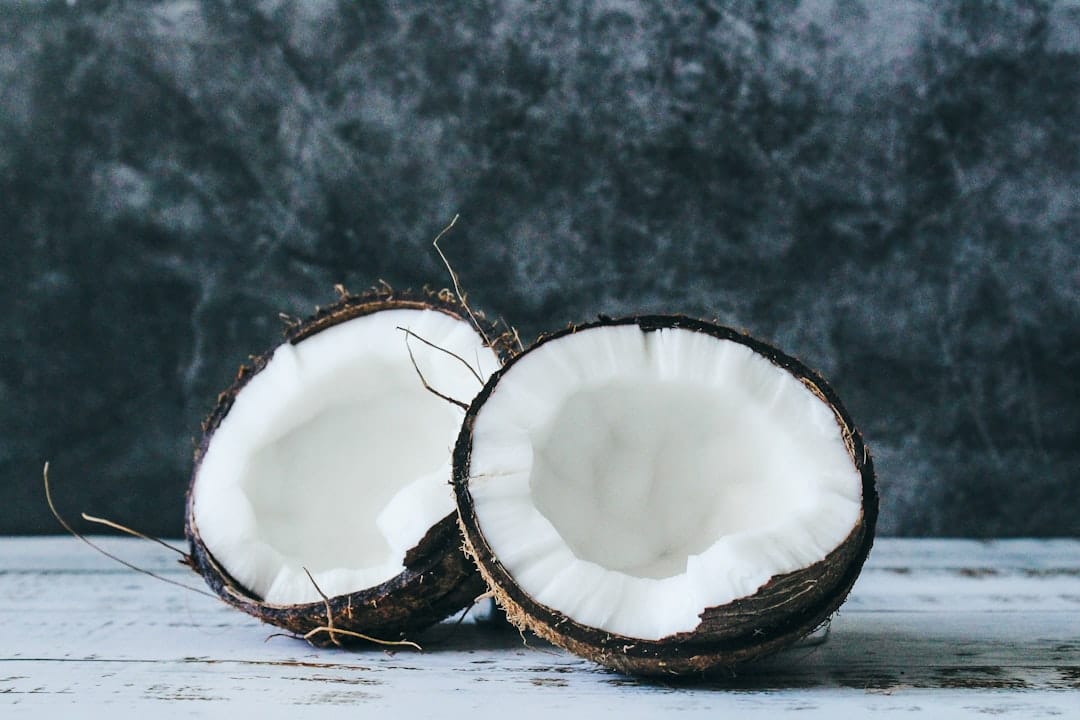 Two halves of a fresh coconut with white flesh on a rustic wooden board