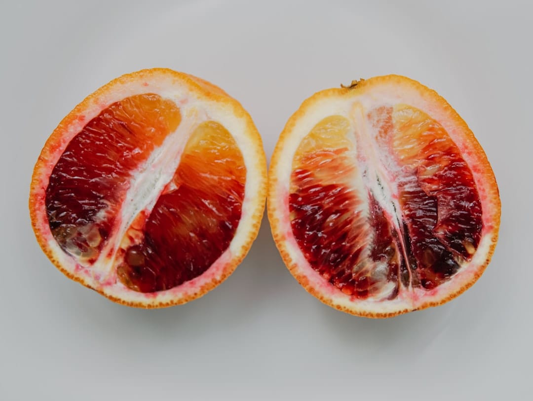 Sliced red citrus scattered over leafy greens in a white bowl