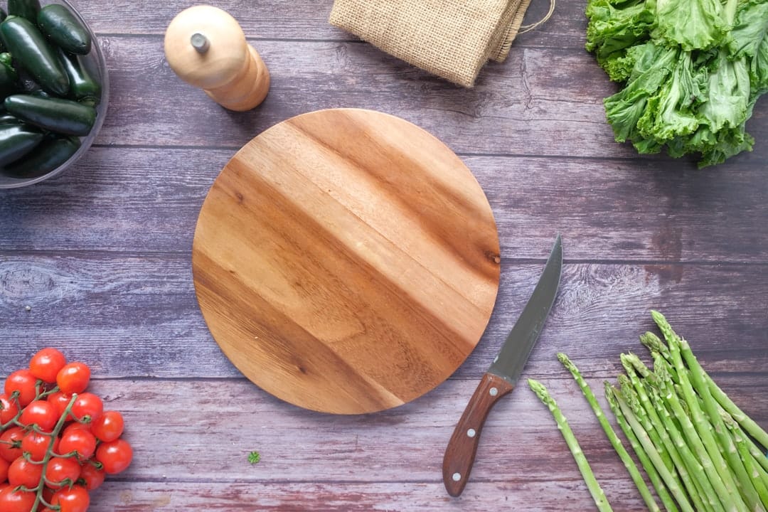 Assorted raw vegetables and herbs arranged on a wooden cutting board in a bright kitchen