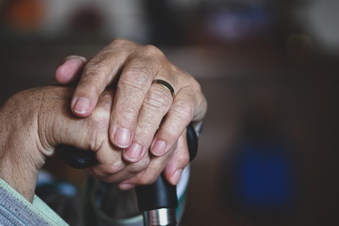 Older person's hands with swollen knuckles resting on a wooden table