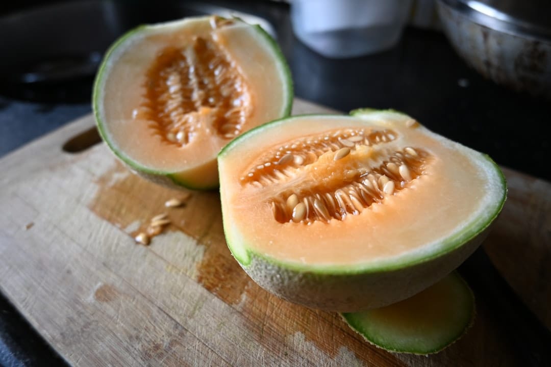 Orange-fleshed cantaloupe cut in half beside a netted rind