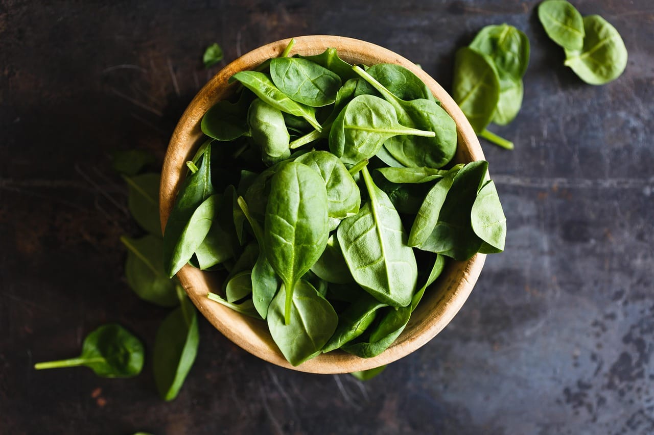 a wooden bowl piled with dark leafy spinach leaves