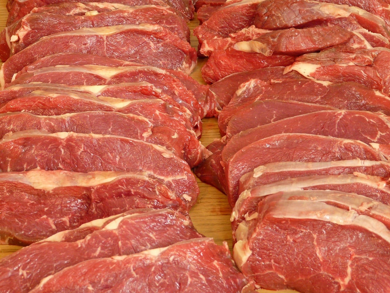 Two raw pork chops resting on a wooden cutting board with fresh herbs