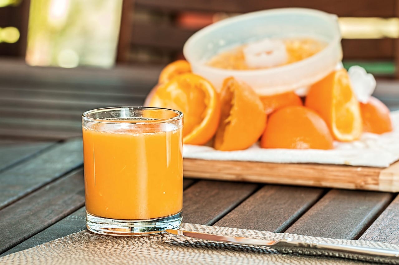 halved cantaloupe beside a glass of fresh orange juice on wood