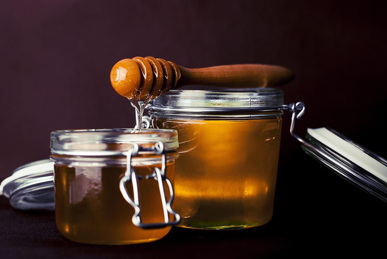 Golden honey dripping from a wooden dipper into an open glass jar