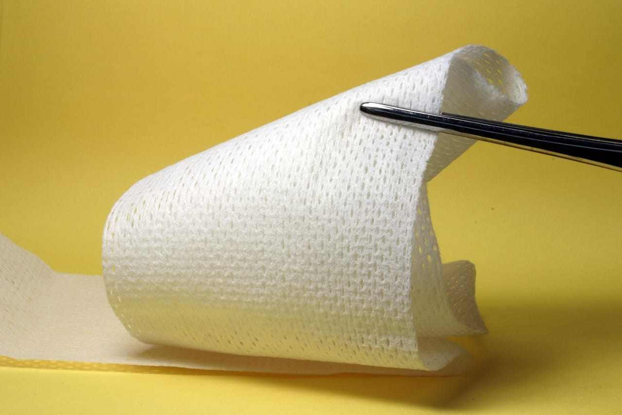 A person pressing white gauze against a small bleeding finger cut