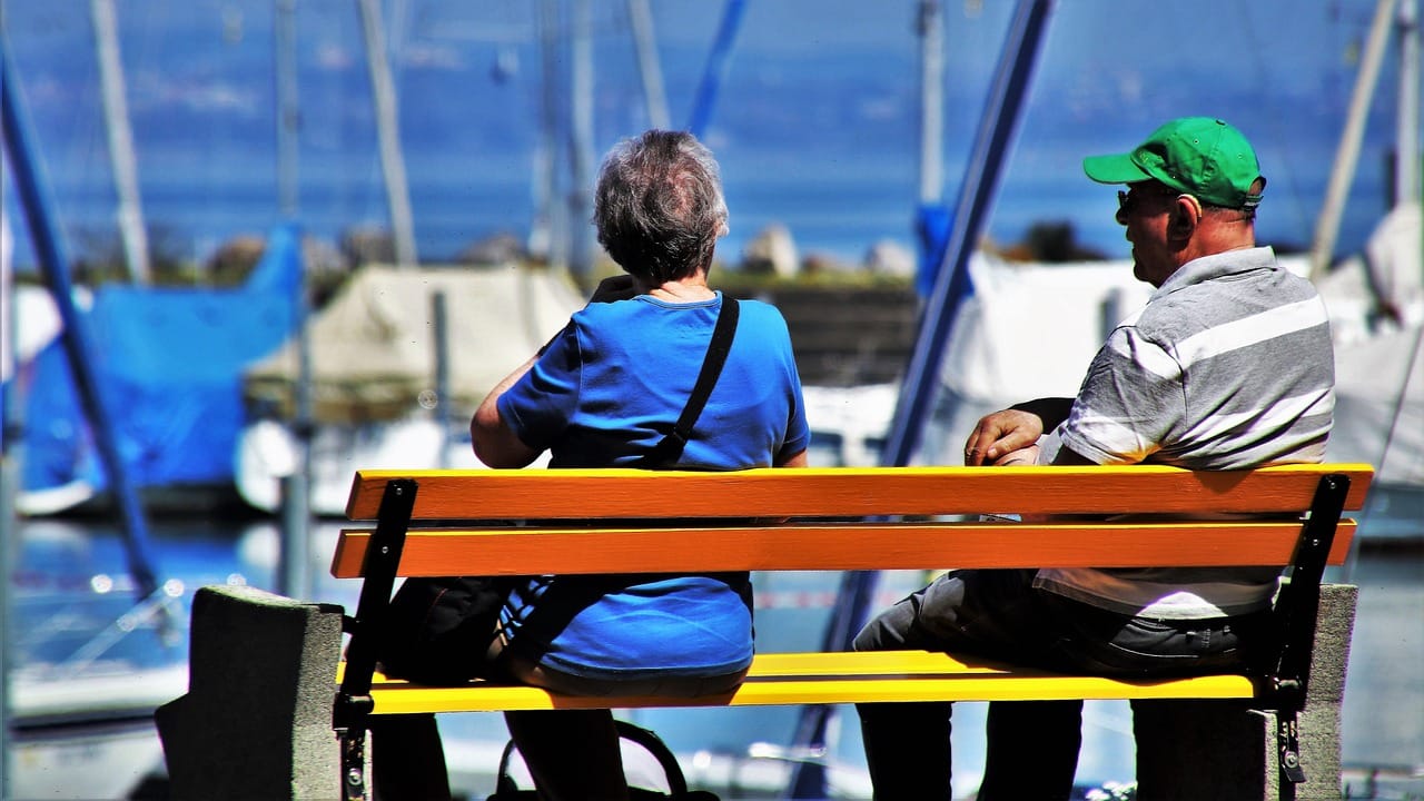 An older couple walking arm in arm along a sunny outdoor path