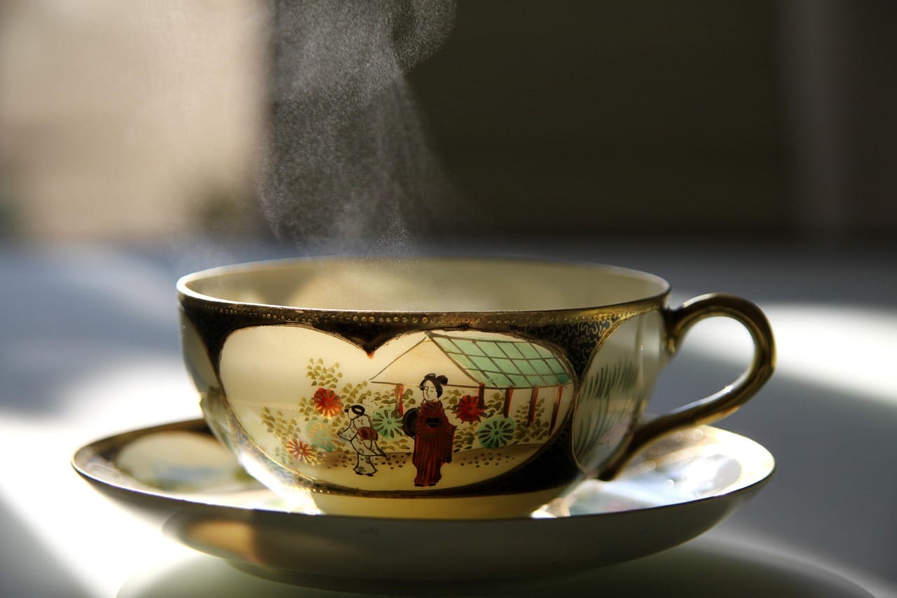 A steaming cup of green tea beside loose tea leaves