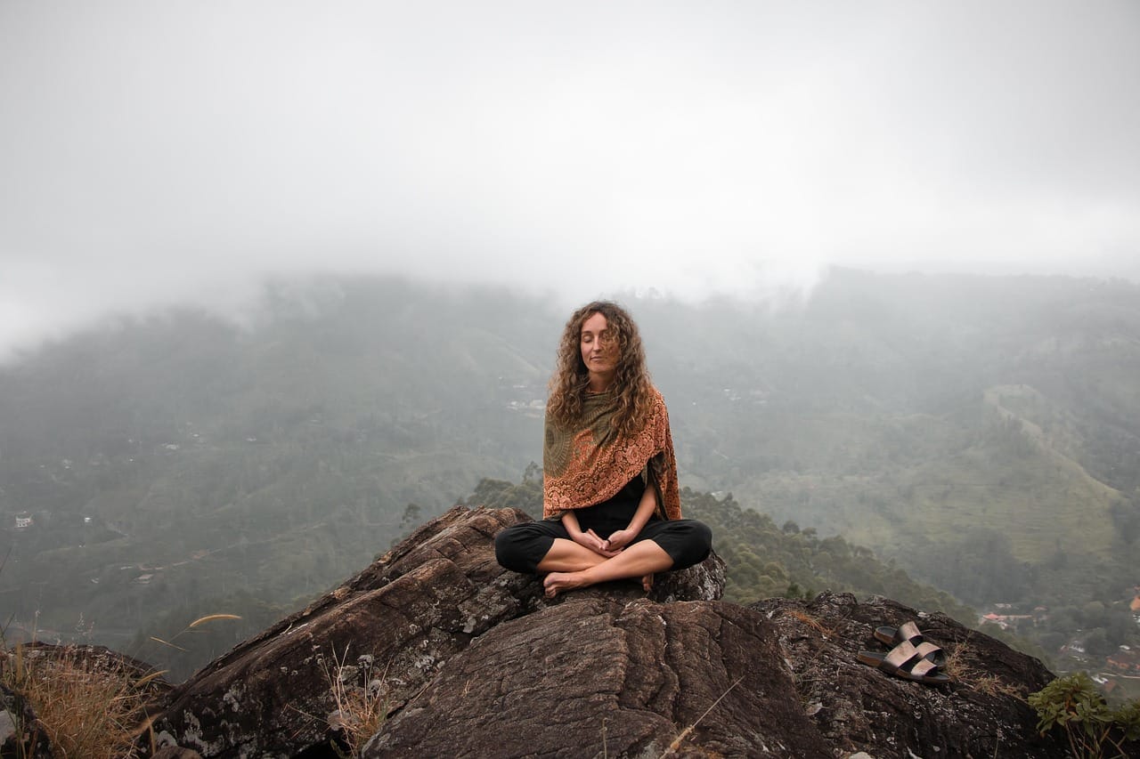 A woman sitting cross-legged on grass with eyes gently closed