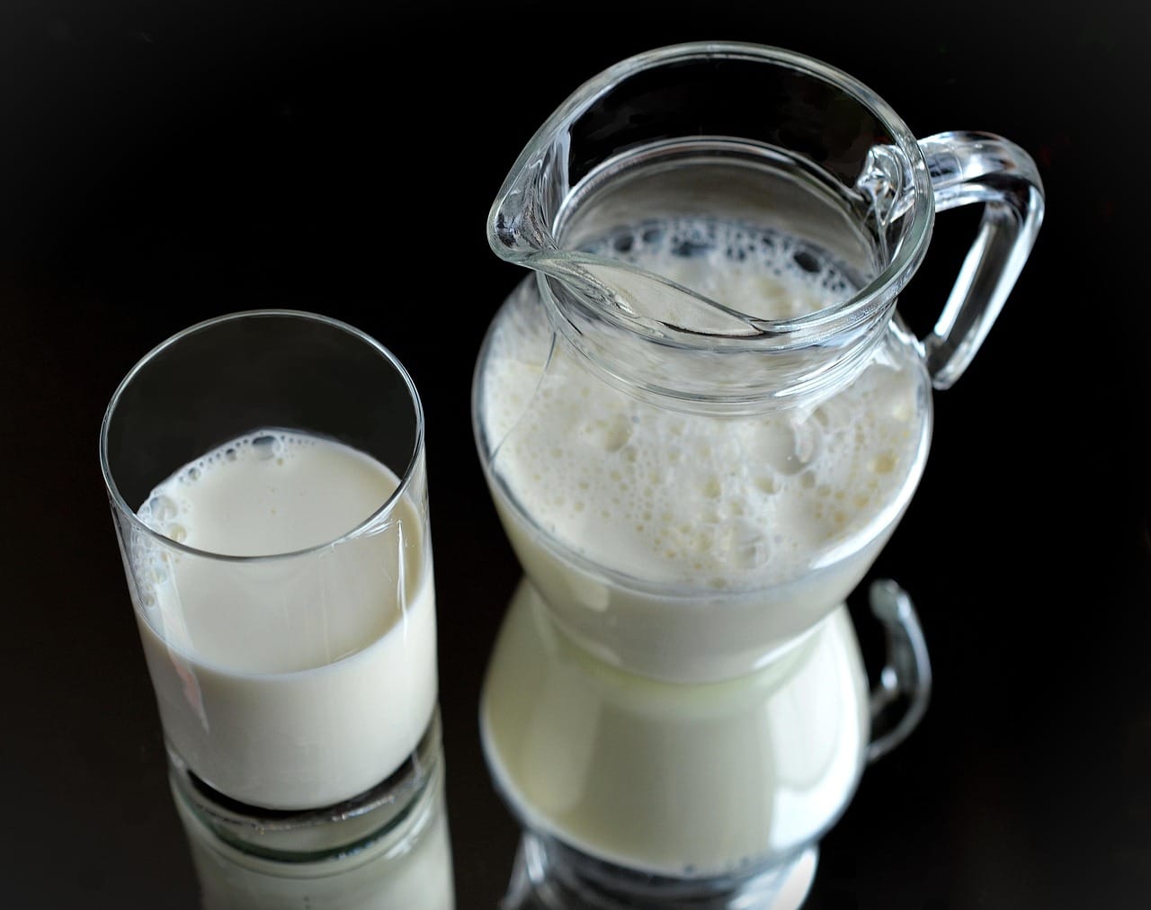 A tall glass of milk beside a jug on a wooden table