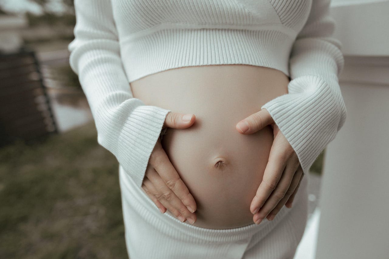 A pregnant woman in a white dress cradling her round belly