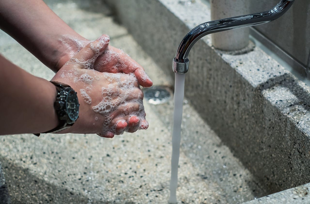 Person lathering soapy hands under a running faucet
