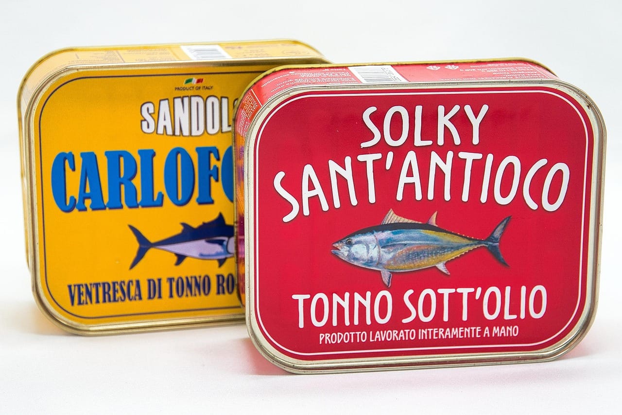 An opened tin of flaked canned tuna resting on a wooden board