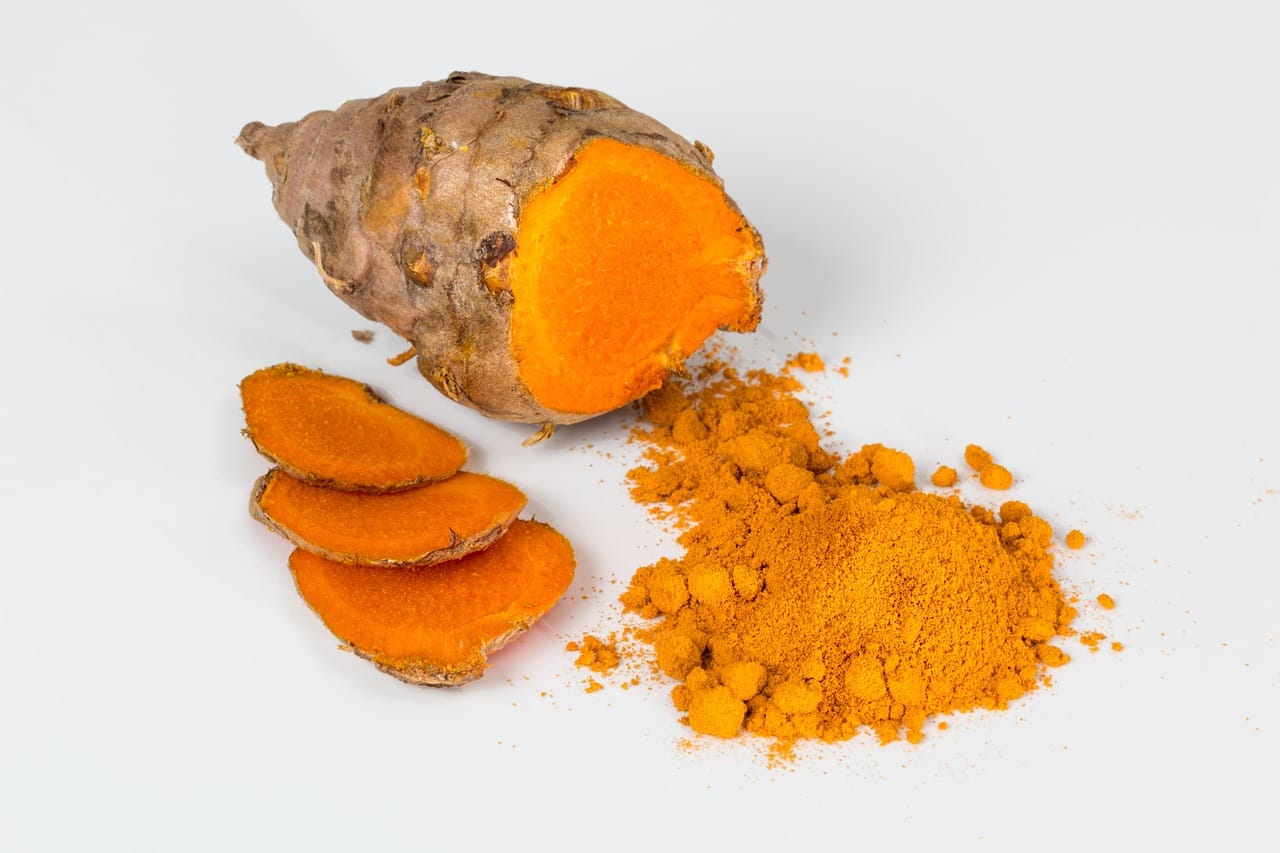 Bright orange turmeric roots and yellow powder arranged on a wooden surface