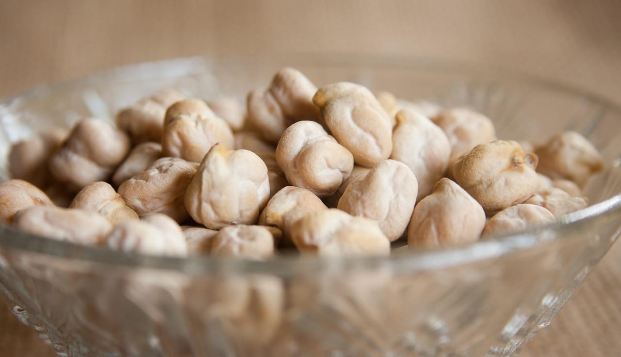 Cooked chickpeas piled in a white ceramic bowl on a wooden table