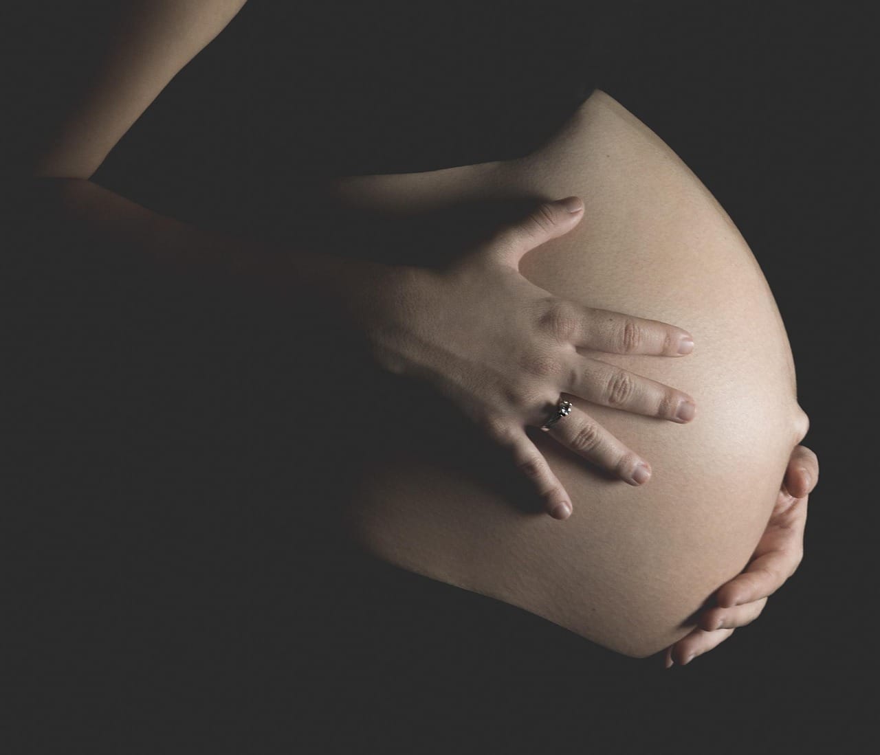 A pregnant woman in a kitchen resting hands on her belly