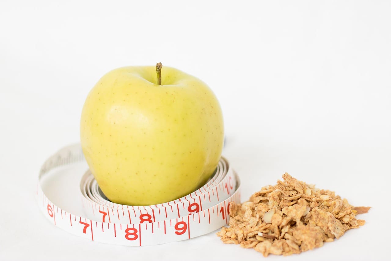 A green apple wrapped in a yellow measuring tape