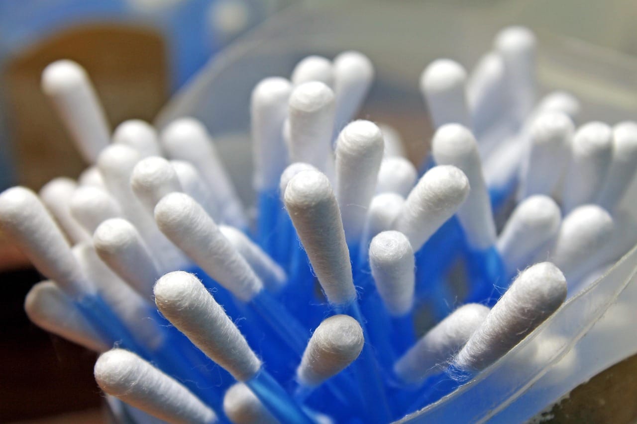 a hand holding a cotton swab beside a small glass dropper bottle