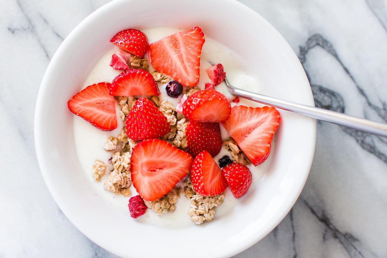 A glass bowl of plain yogurt topped with fresh blueberries