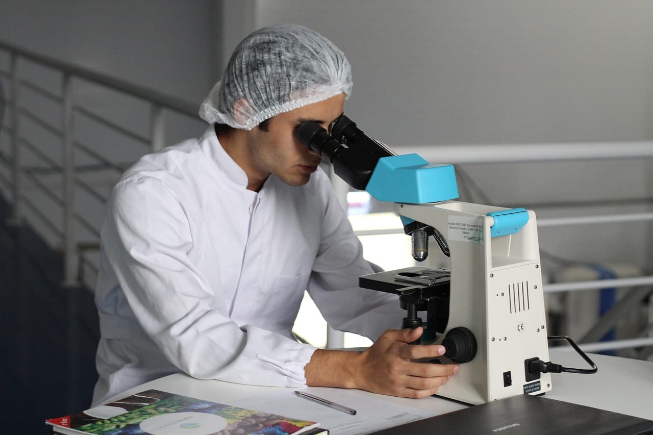 researcher in a white coat looking into a microscope in a lab