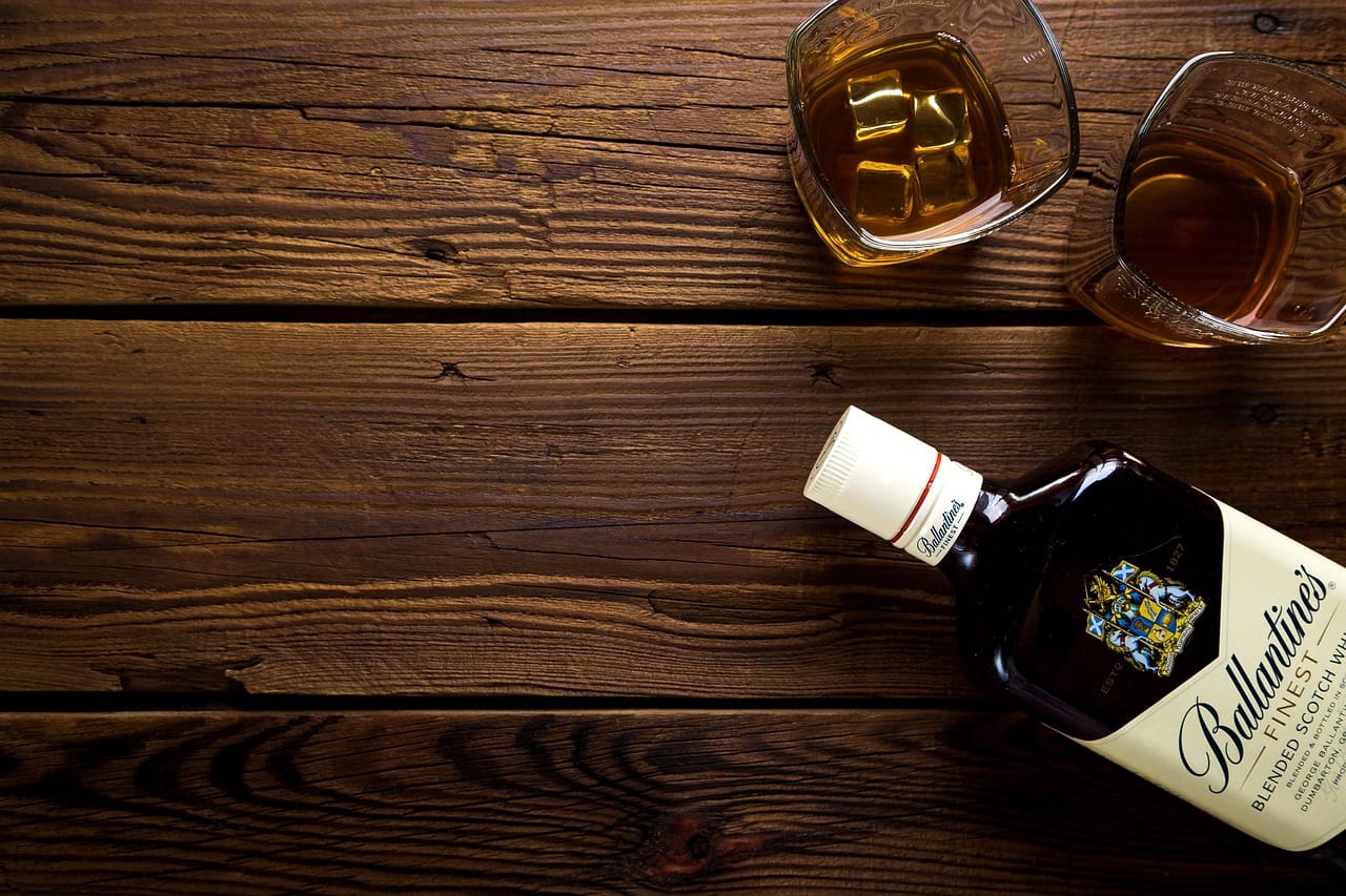 Amber whiskey poured into a glass beside a bottle on wood