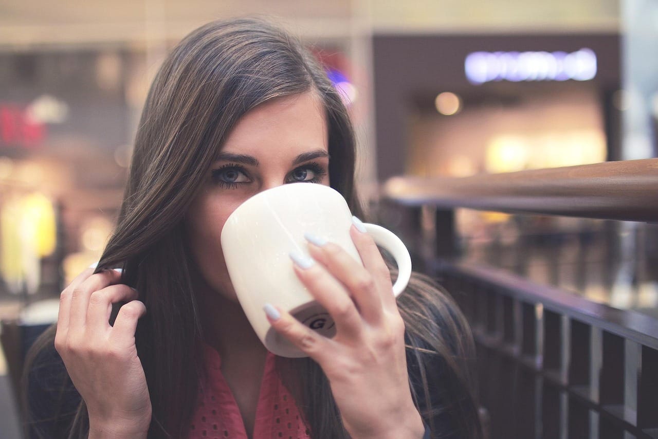 A woman in a sunlit kitchen sipping from a warm mug