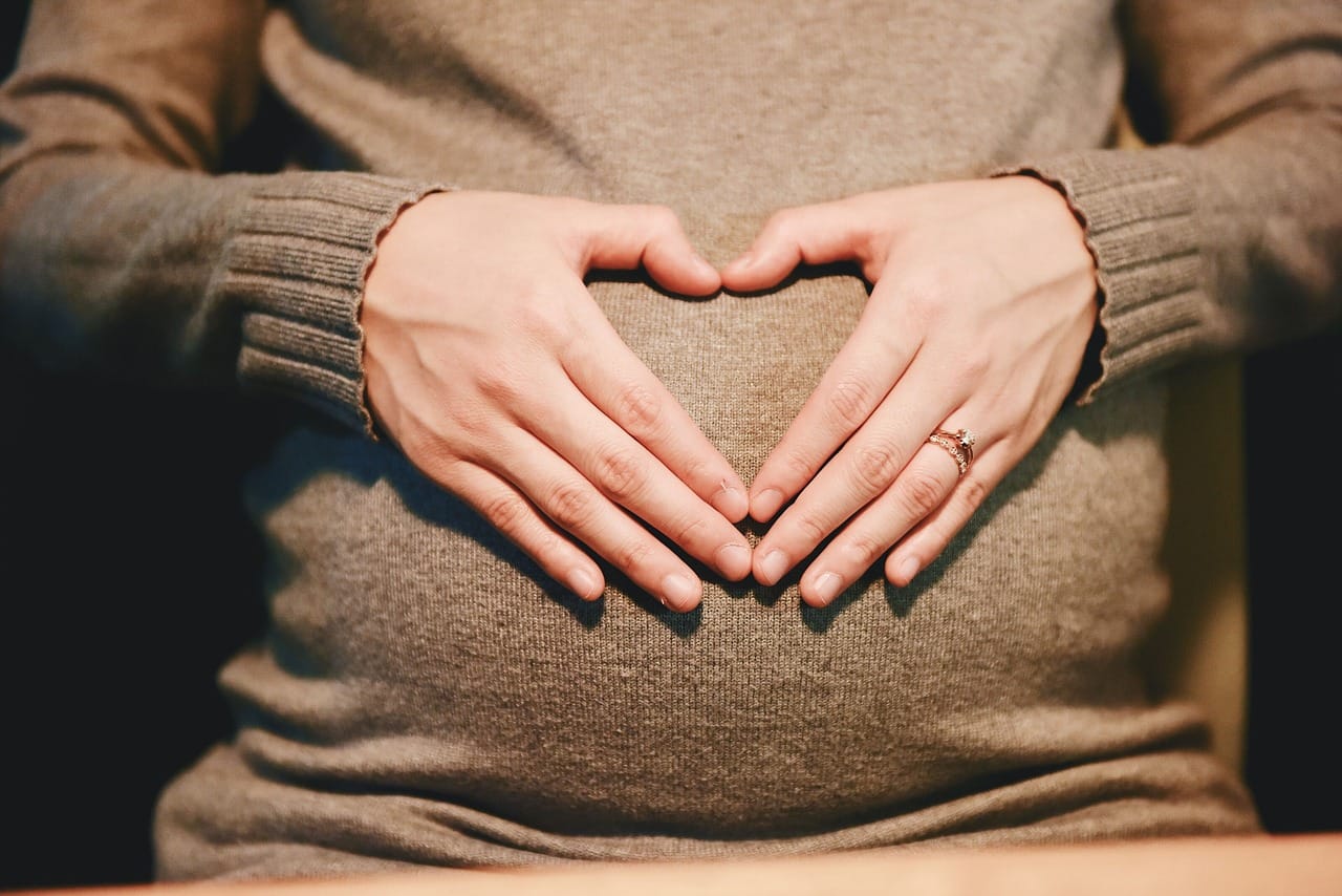 A pregnant woman cradling a warm mug near a sunlit window
