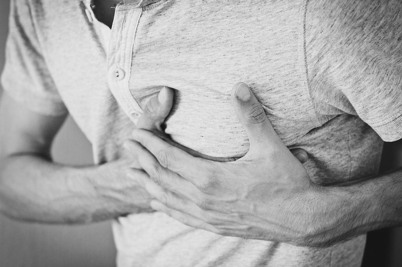 A man grimacing and pressing a hand against his upper chest