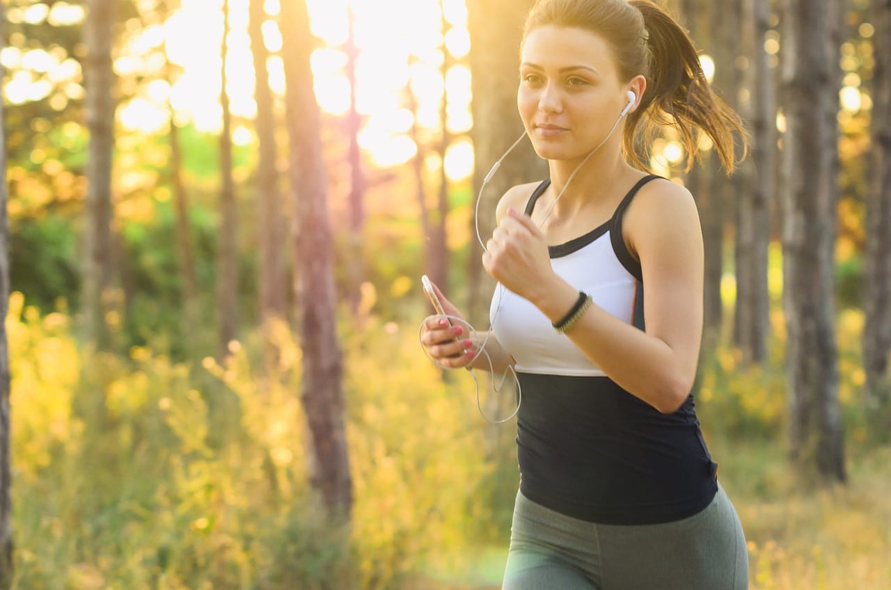 Smiling woman running along a tree-lined park path in morning light