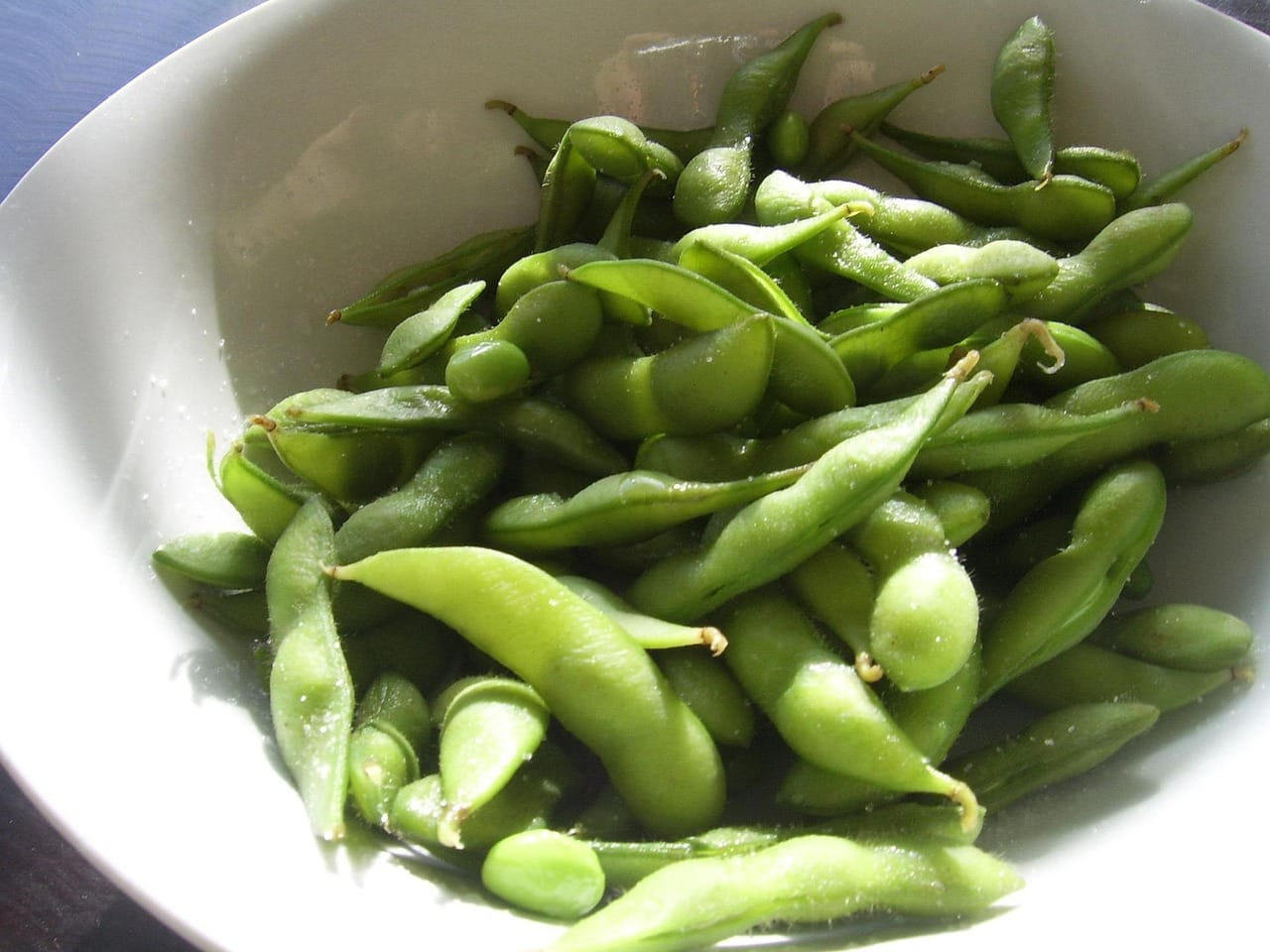 Green soybean pods spilling from a wooden bowl on a table