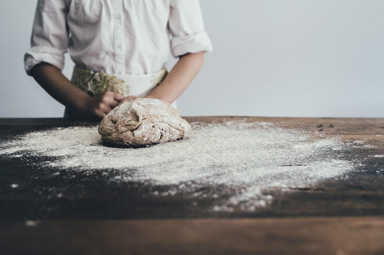A baker pressing sticky dough on a floured wooden countertop