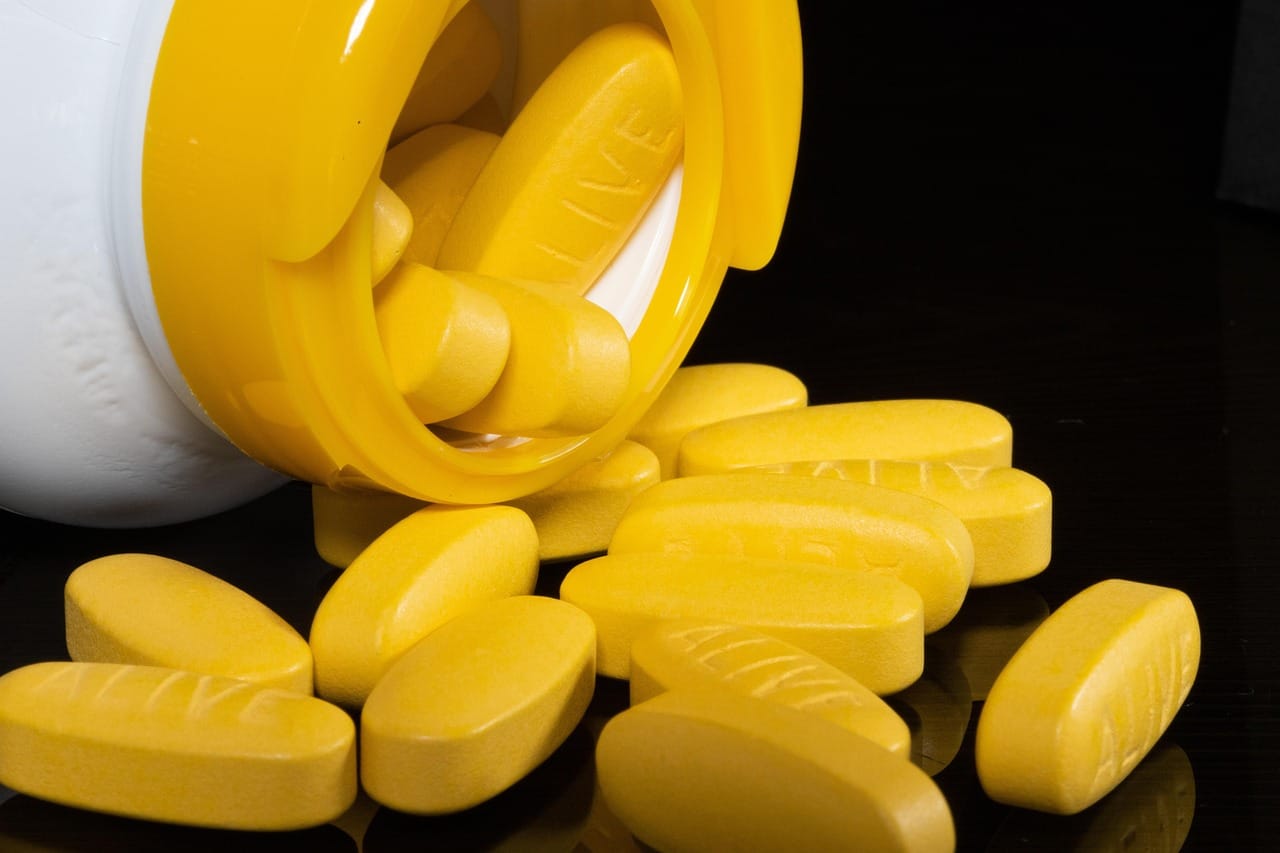 Golden softgel capsules spilling from a white bottle onto a pale table