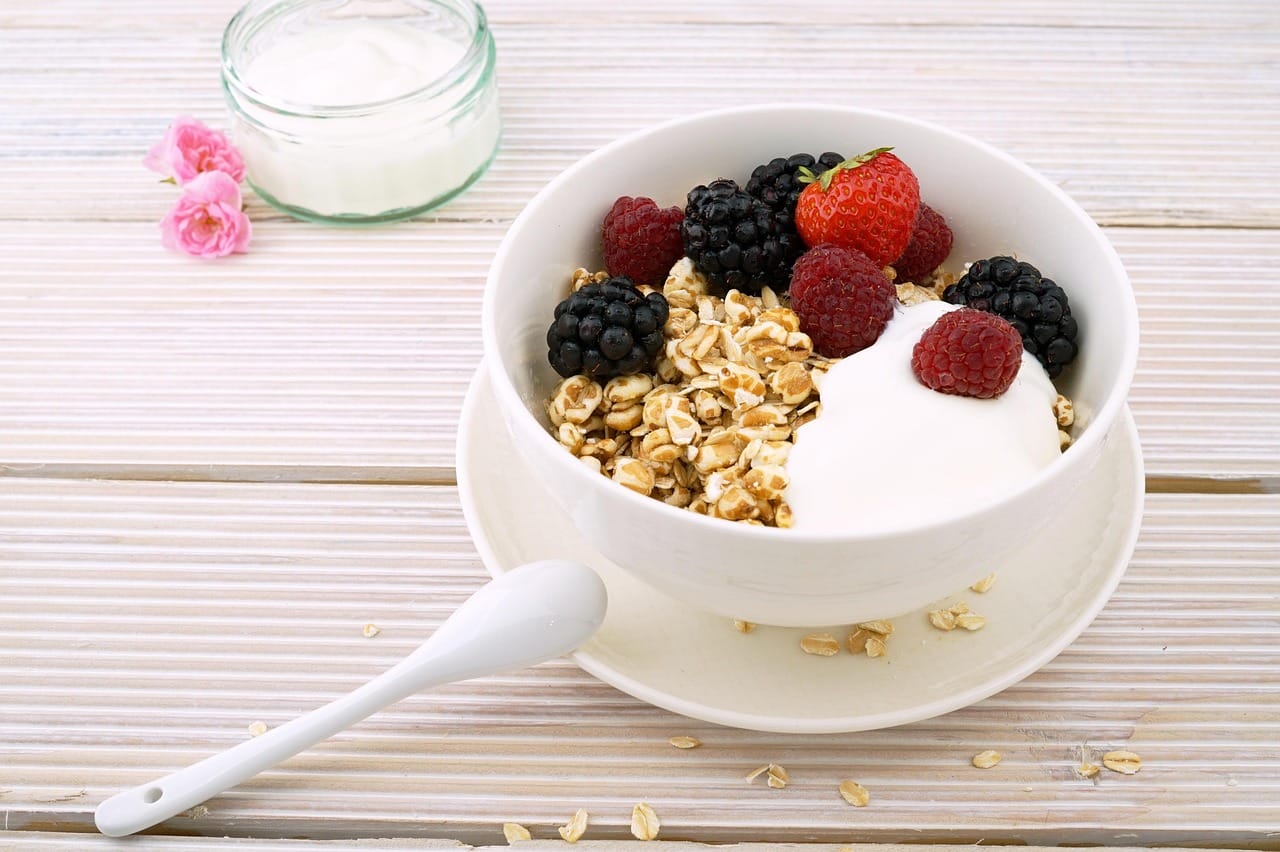 A white ceramic bowl of plain yogurt topped with berries