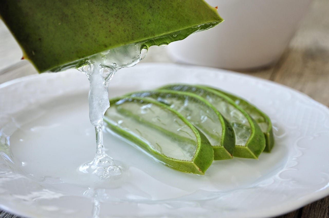 A cut aloe vera leaf oozing clear gel on a wooden board