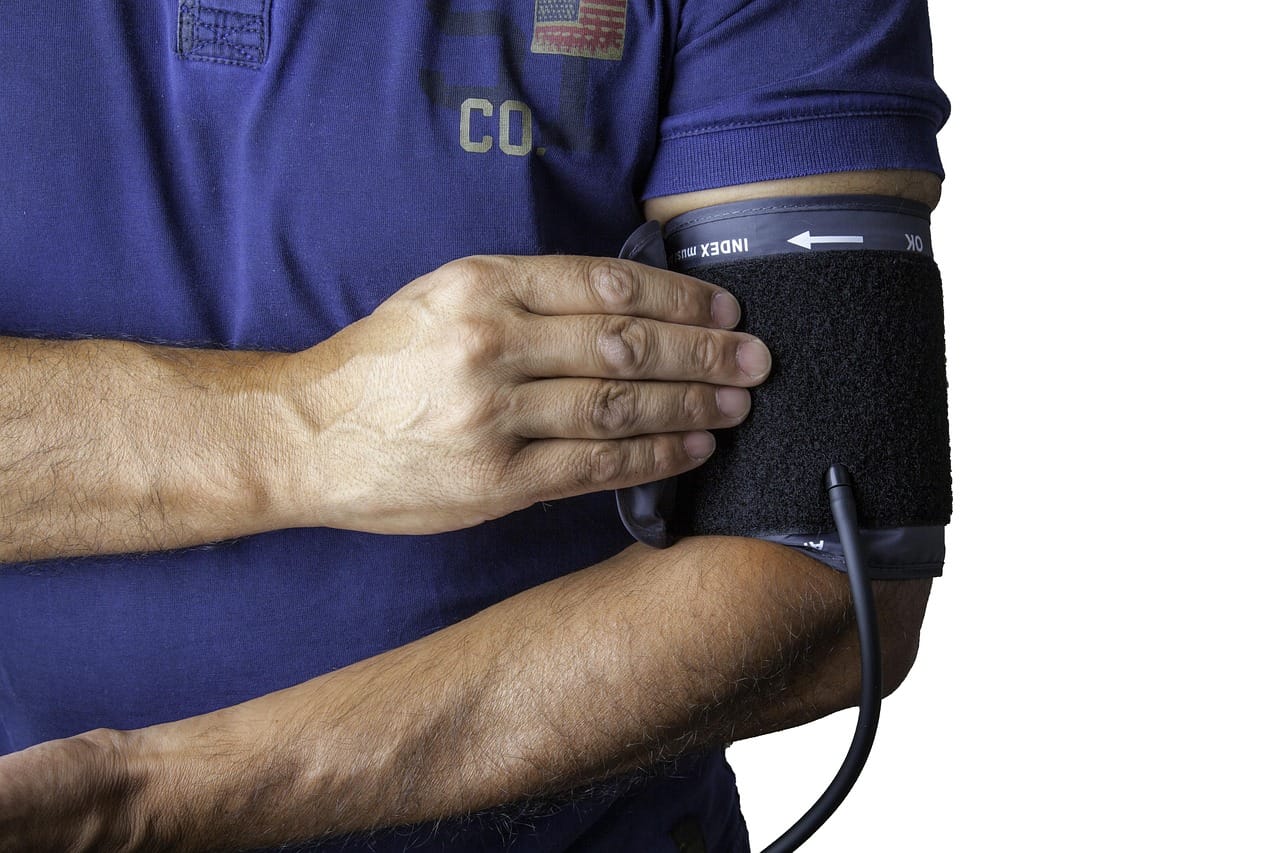 Home blood pressure cuff and monitor resting on a table beside a person's arm