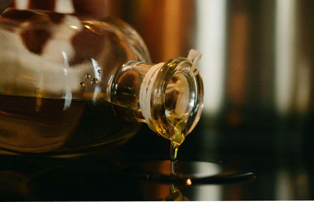 Golden olive oil drizzling from a glass bottle onto greens